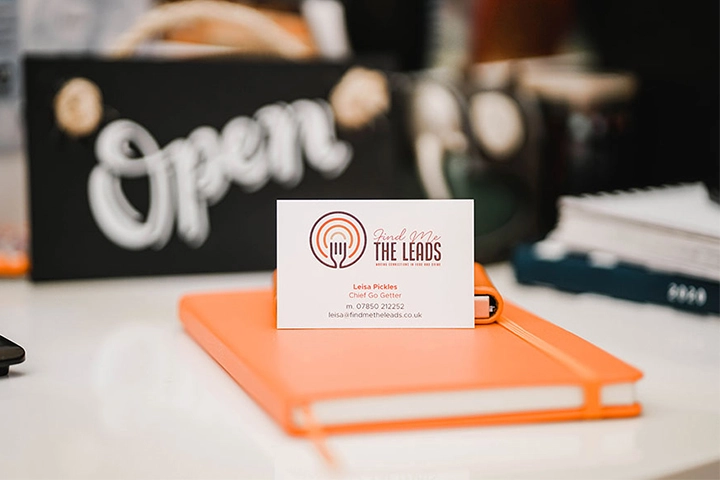 Find Me The Leads business card standing on an orange notebook