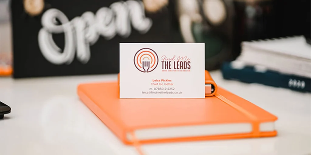 Find Me The Leads business card sitting on an orange notebook